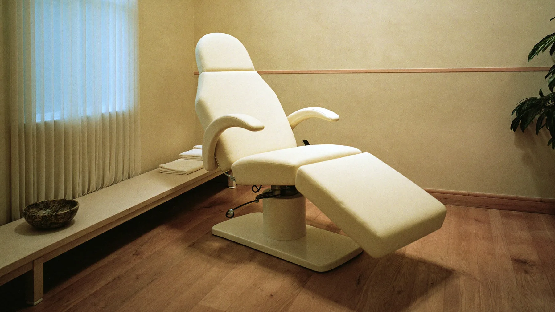 Una sala de tratamiento privada en Redefyn Aesthetics, el sillón elevado y toallas dobladas en una banca junto a la pared